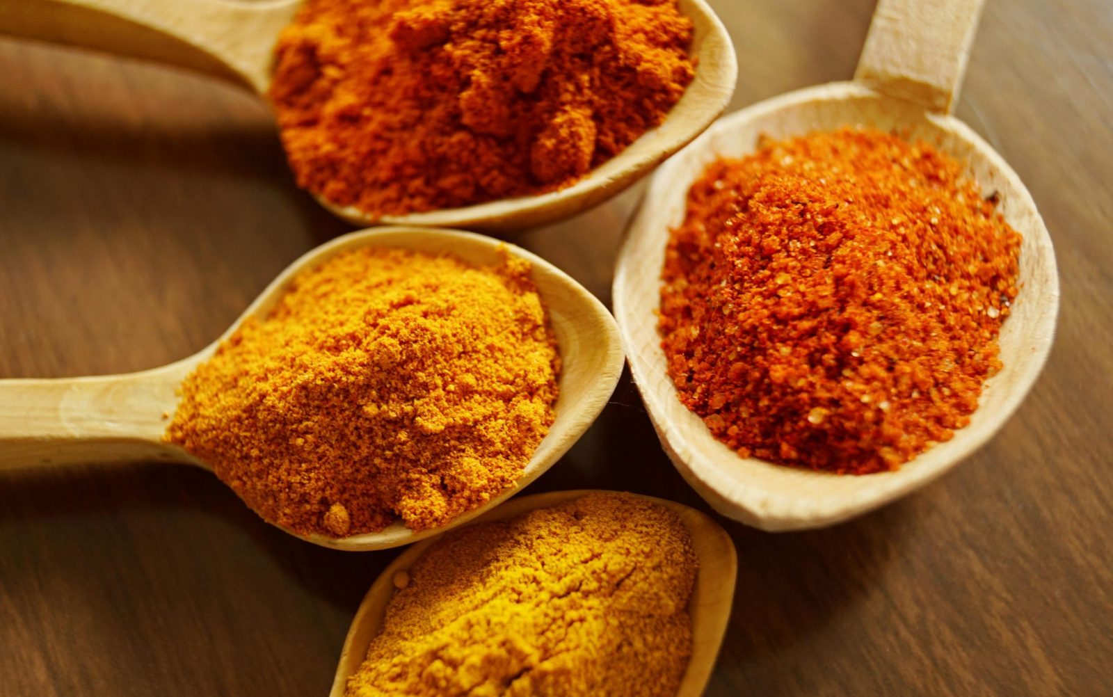 Close-up of vibrant spices like turmeric and chili powder in wooden spoons.